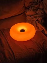 Luminária Donut laranja acesa sobre uma cama